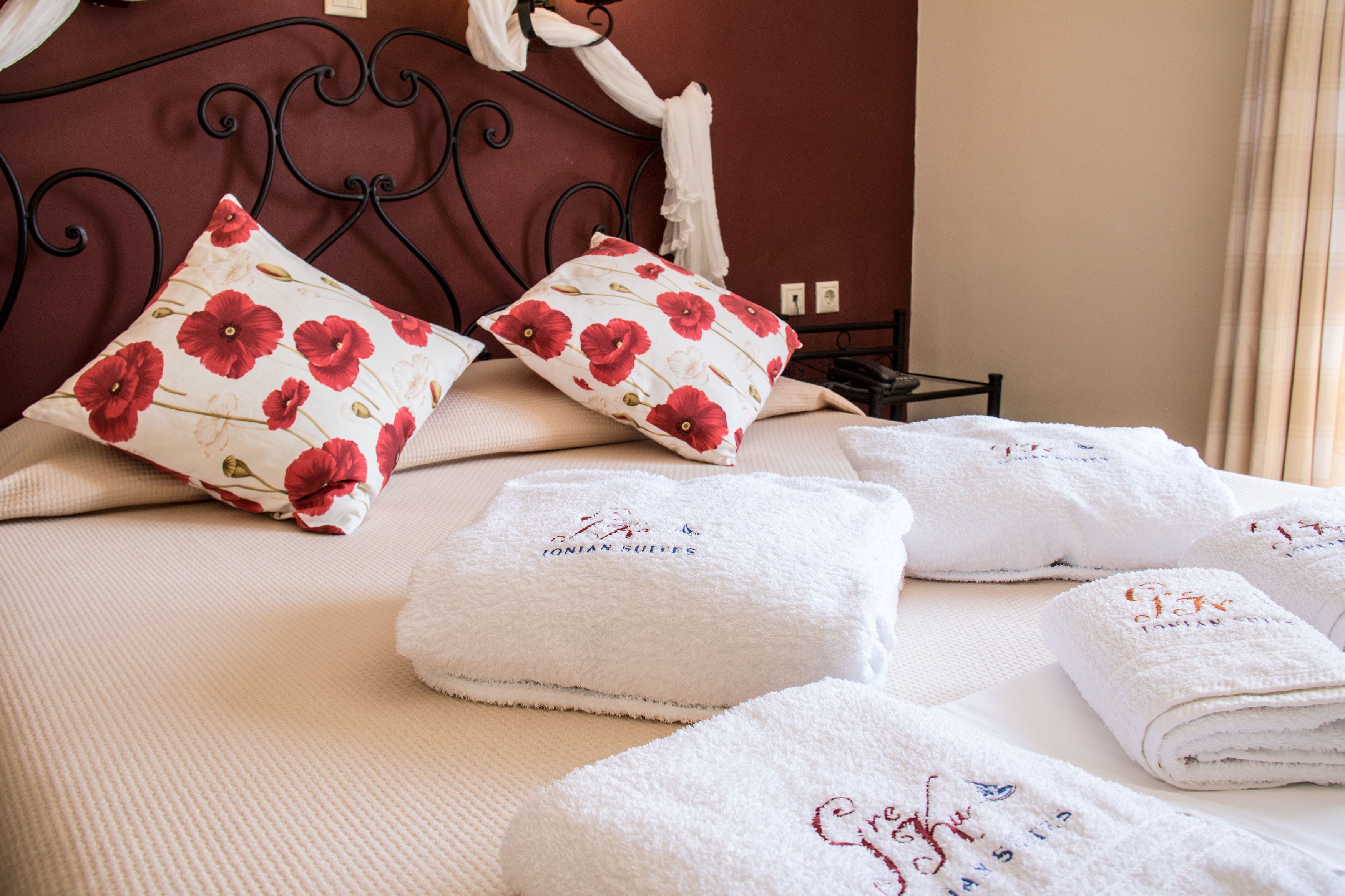 Una cama bien tendida con almohadillas florales, una mesita de noche y toallas dobladas con texto bordado.