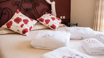 A neatly made bed with floral pillows, a bedside table, and neatly folded towels with embroidered text.