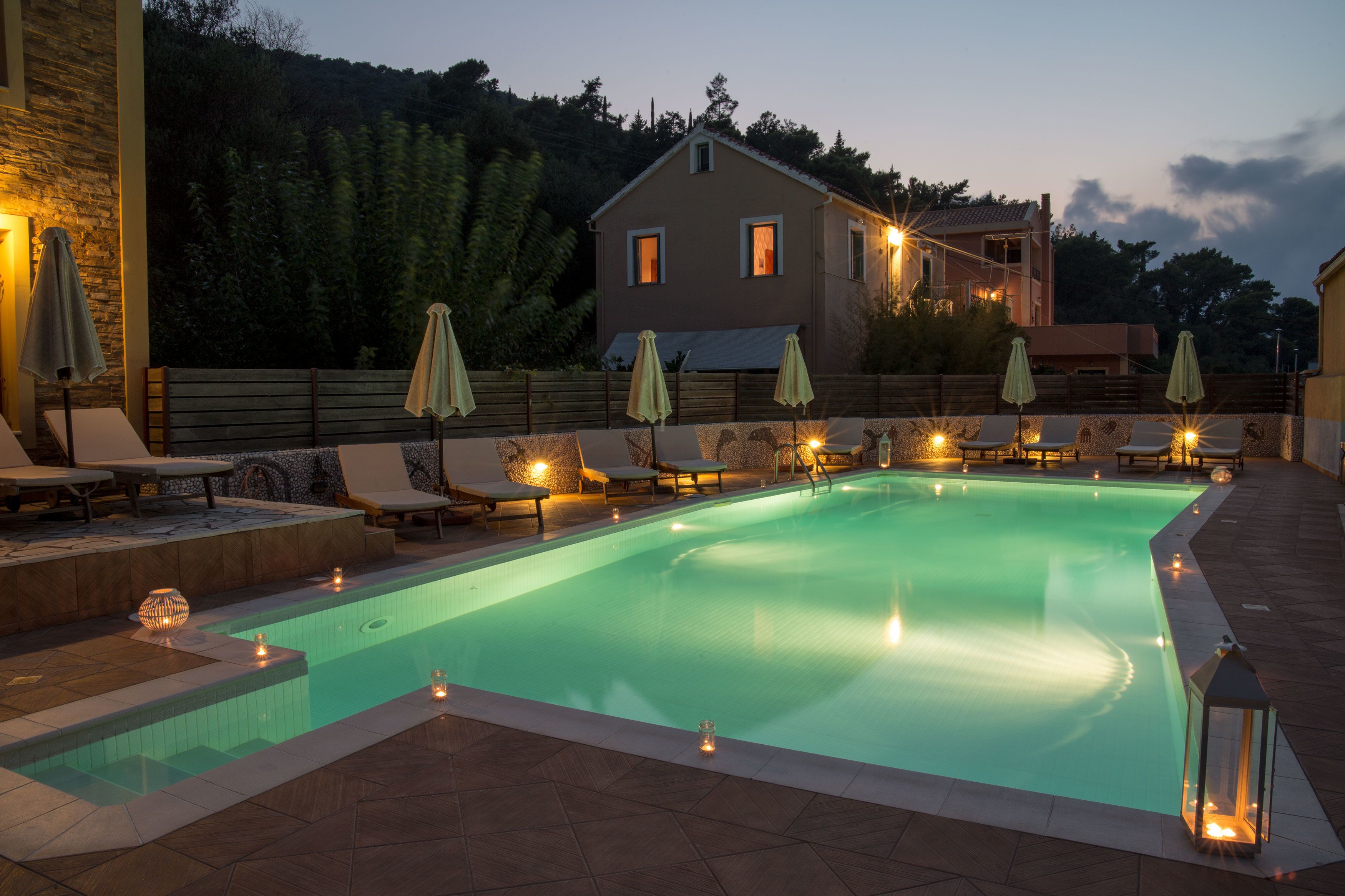 Una piscina con sillones de descanso y sombrillas, rodeada por un muro de piedra y una casa.