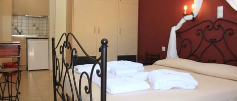 A bedroom with a bed, a small kitchenette, and a bathroom visible in the background.
