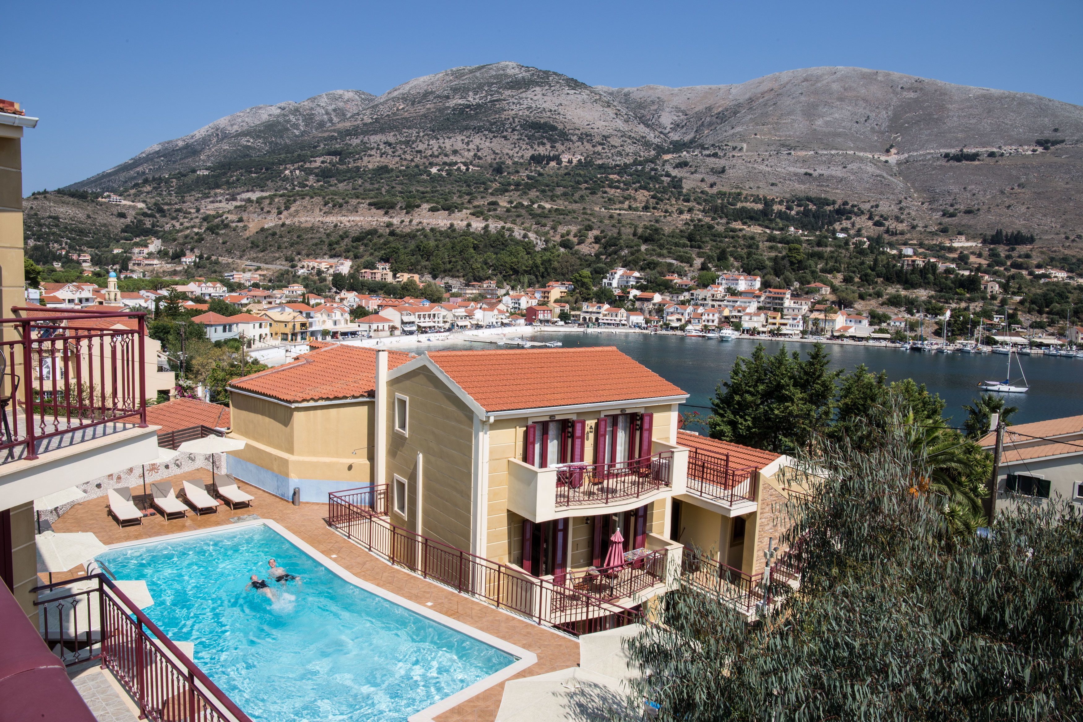 A hotel with a swimming pool, balconies, and a view of a lake and mountains.