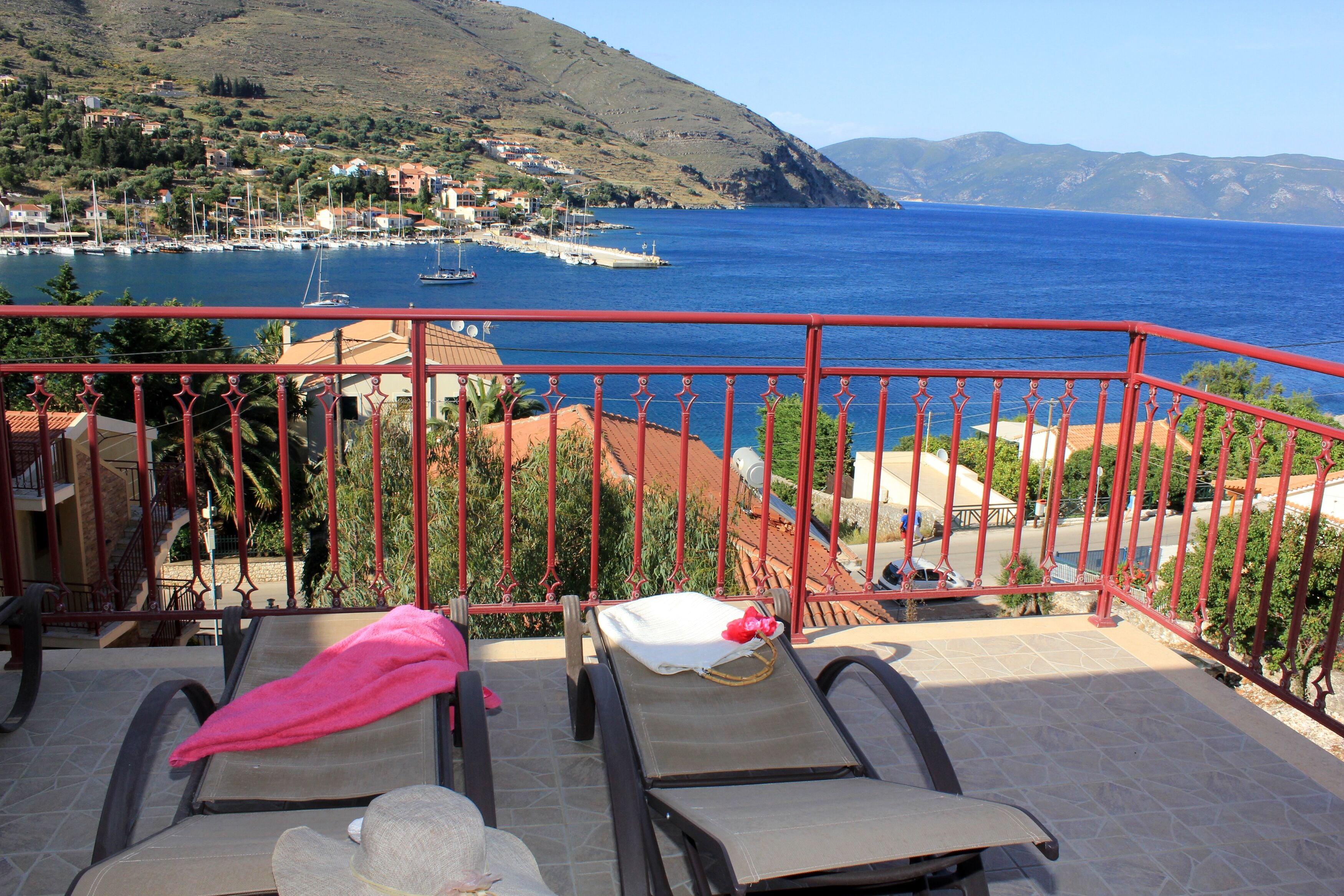 A balcony with two sun loungers, one with a pink towel, overlooking a coastal town and the sea.