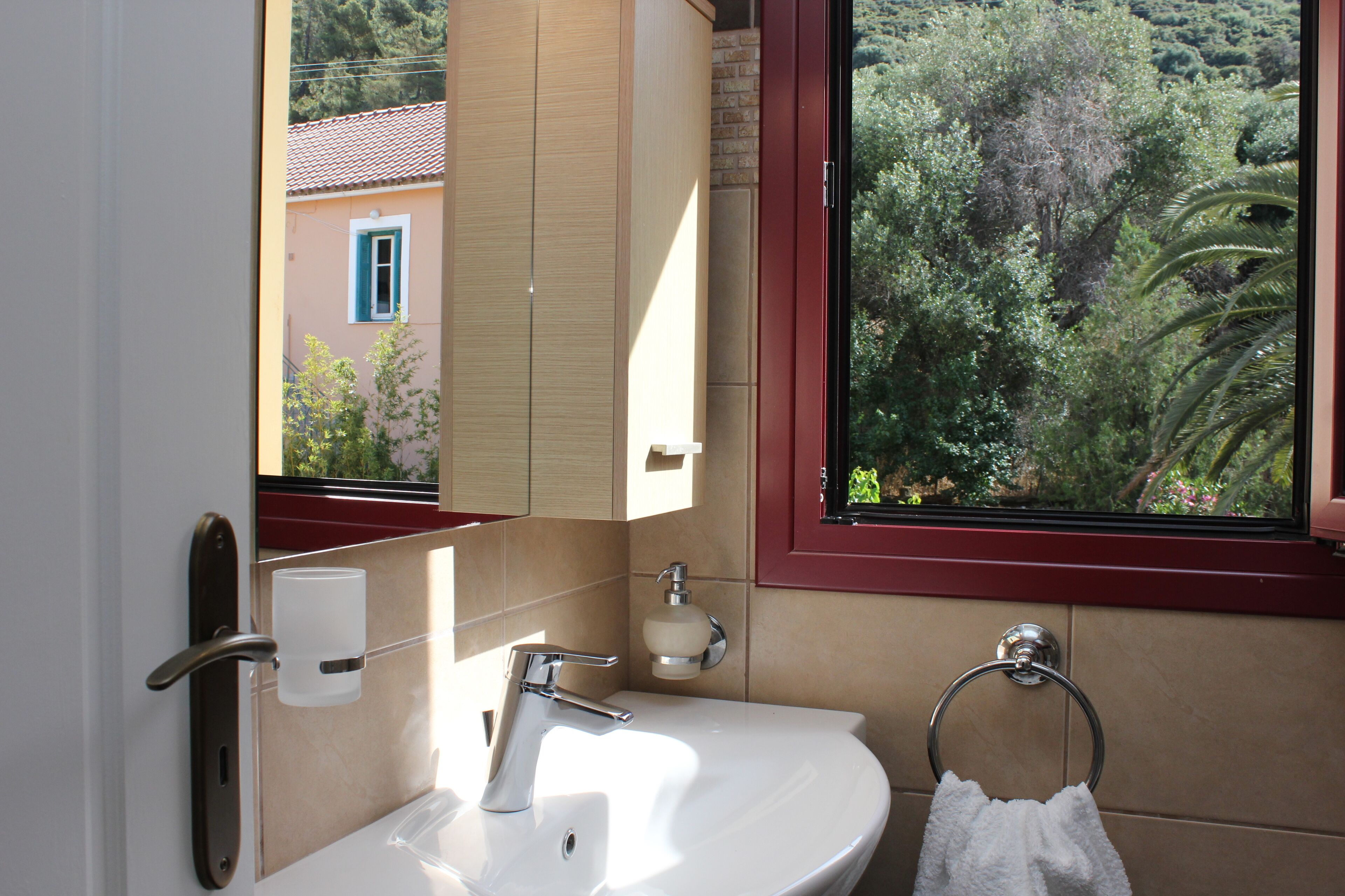 Une salle de bain avec un lavabo blanc, un miroir, un porte-serviettes et une fenêtre donnant sur un paysage verdoyant.