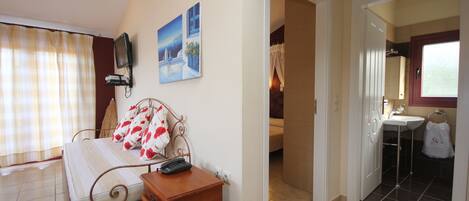 A bedroom with a bed, bedside table, and a television. There is a bathroom with a sink and a towel hanging on the door.