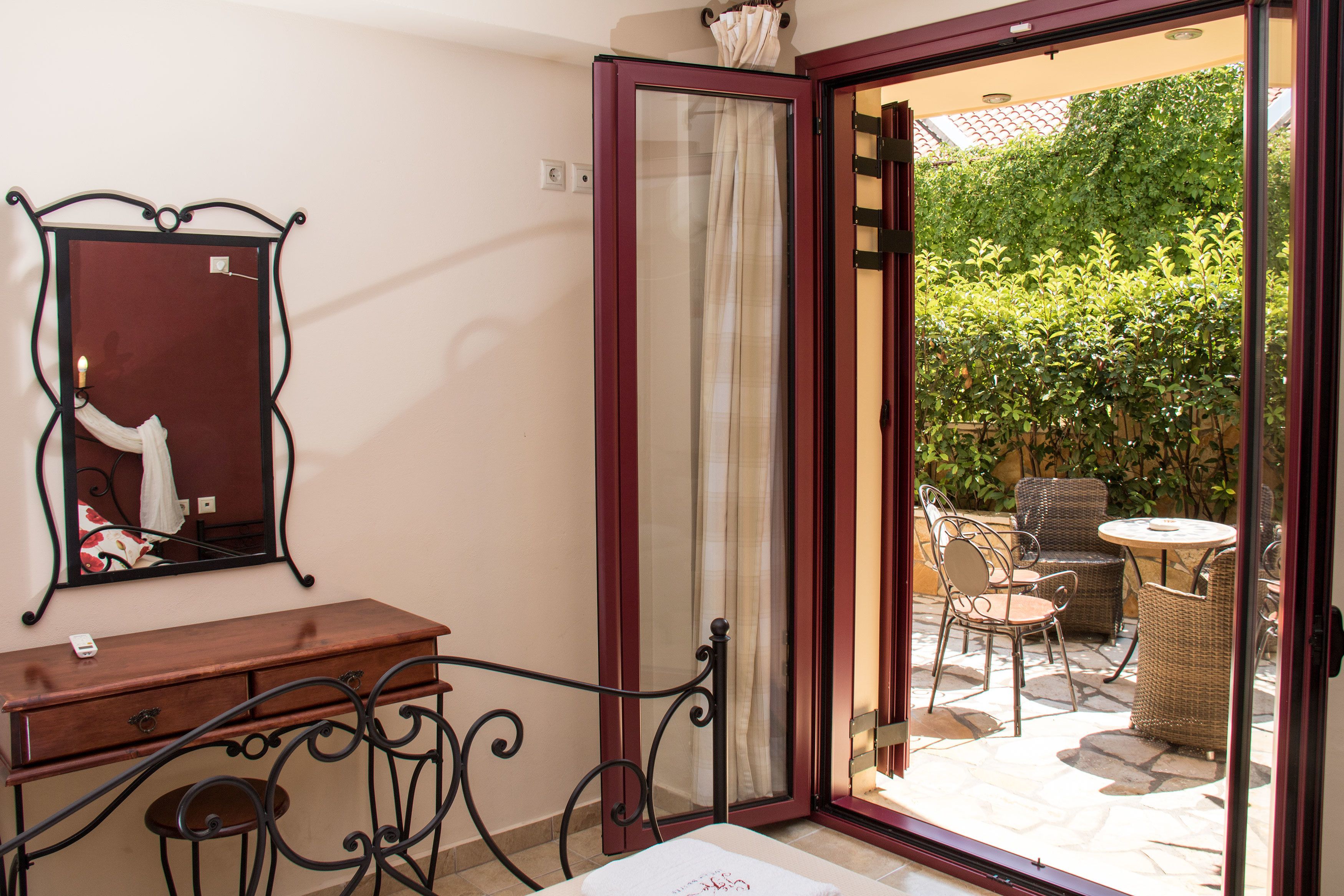 Una habitación con cómoda de madera, espejo y puerta corrediza de vidrio que da a un patio exterior con mobiliario de mimbre y vistas a un jardín.