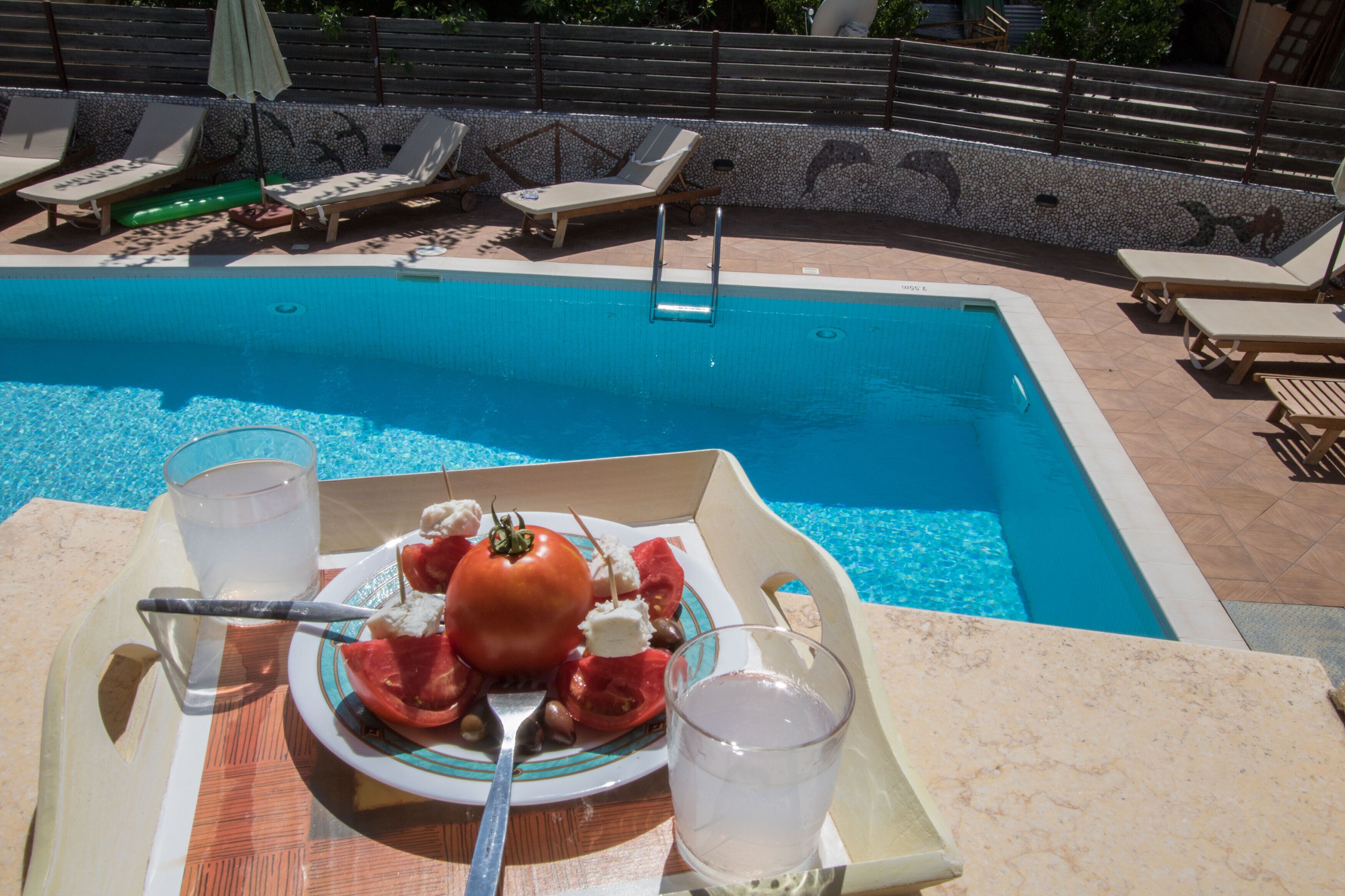 A poolside table with a plate of food, a glass of water, and a drink tray.