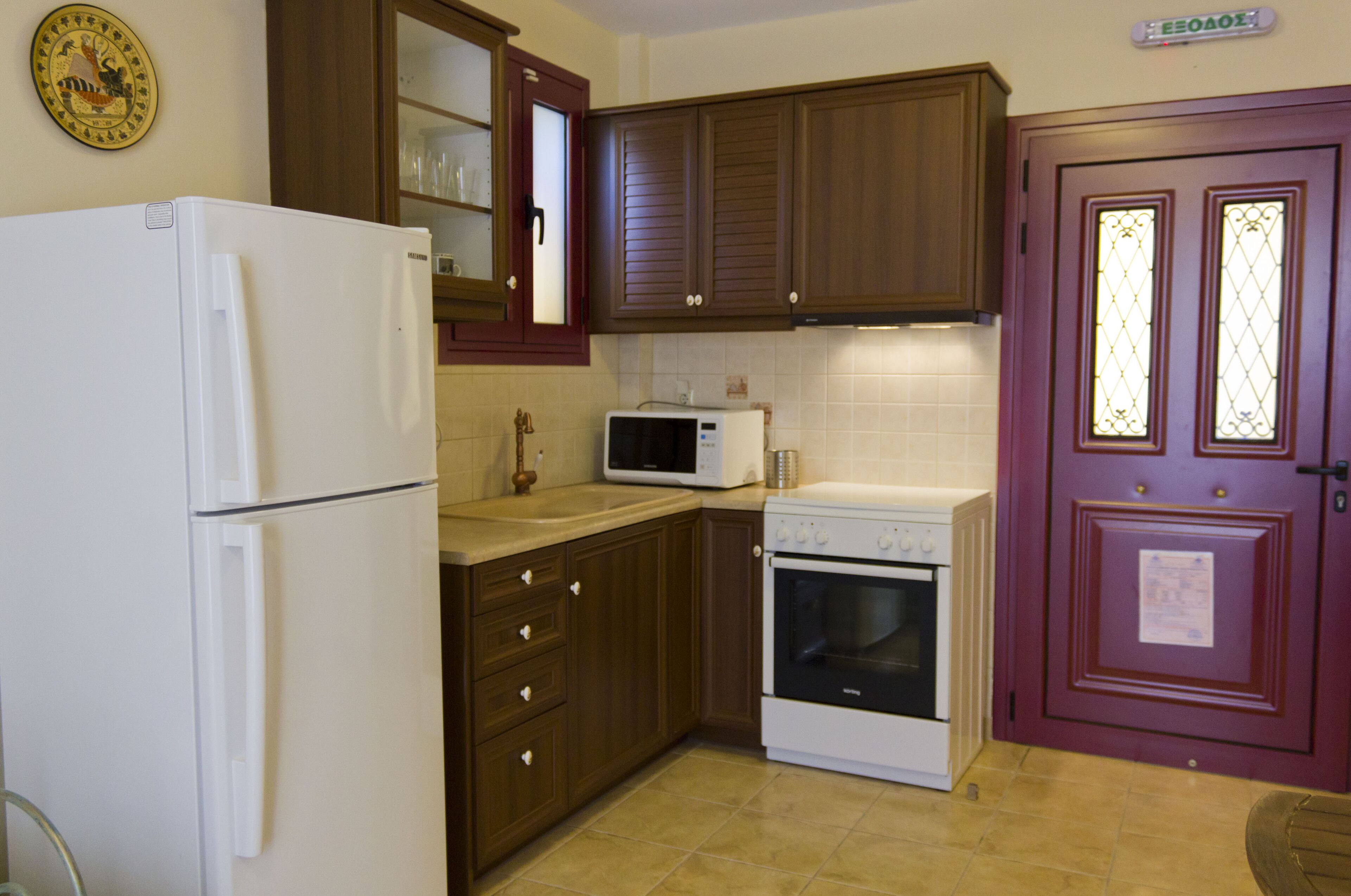 A kitchen with a refrigerator, microwave, oven, wooden cabinets, and a door with glass panels.