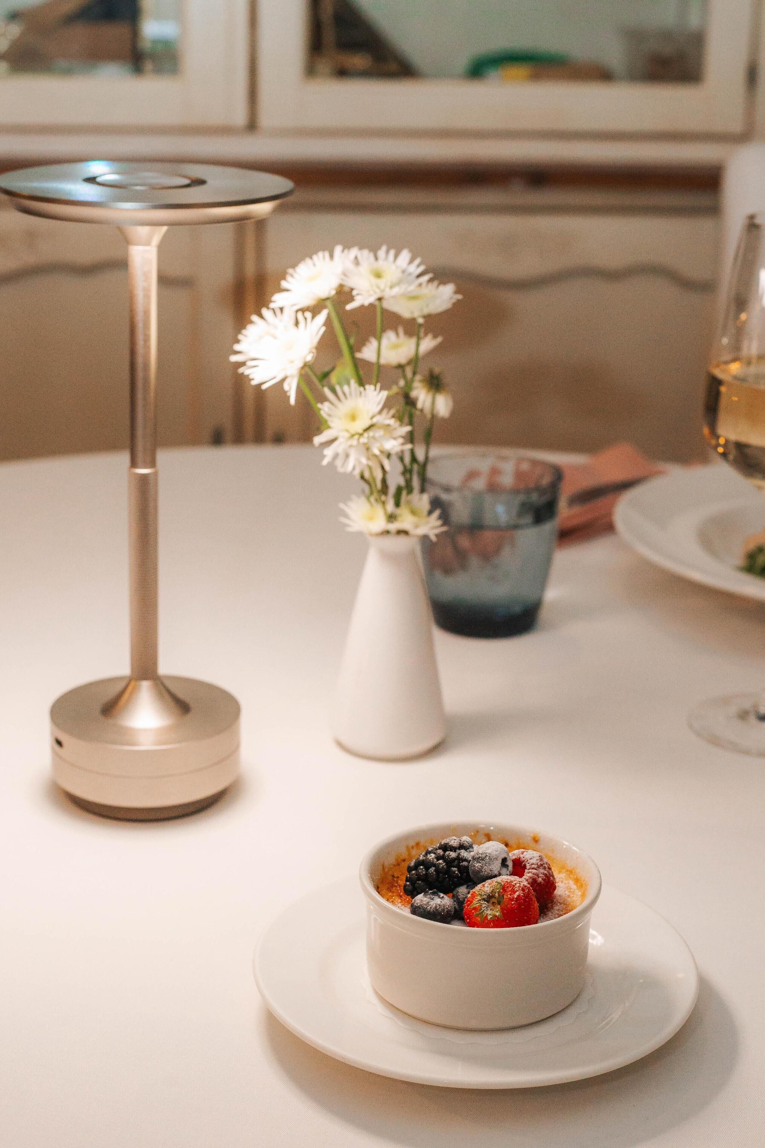 Un postre sobre un plato blanco, con un jarrón de flores blancas y un candelabro al fondo.