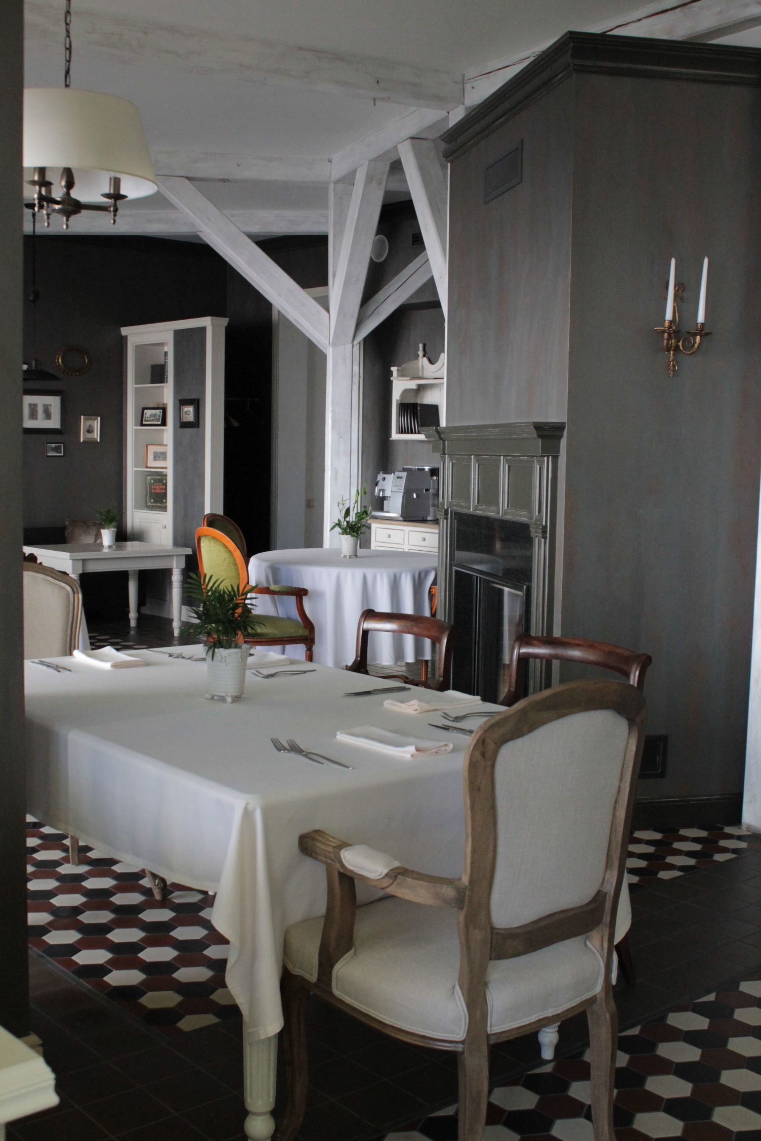 A dining area with a large table, chairs, a chandelier, and a kitchen in the background.