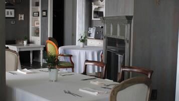 A dining area with a large table, chairs, a chandelier, and a kitchen in the background.