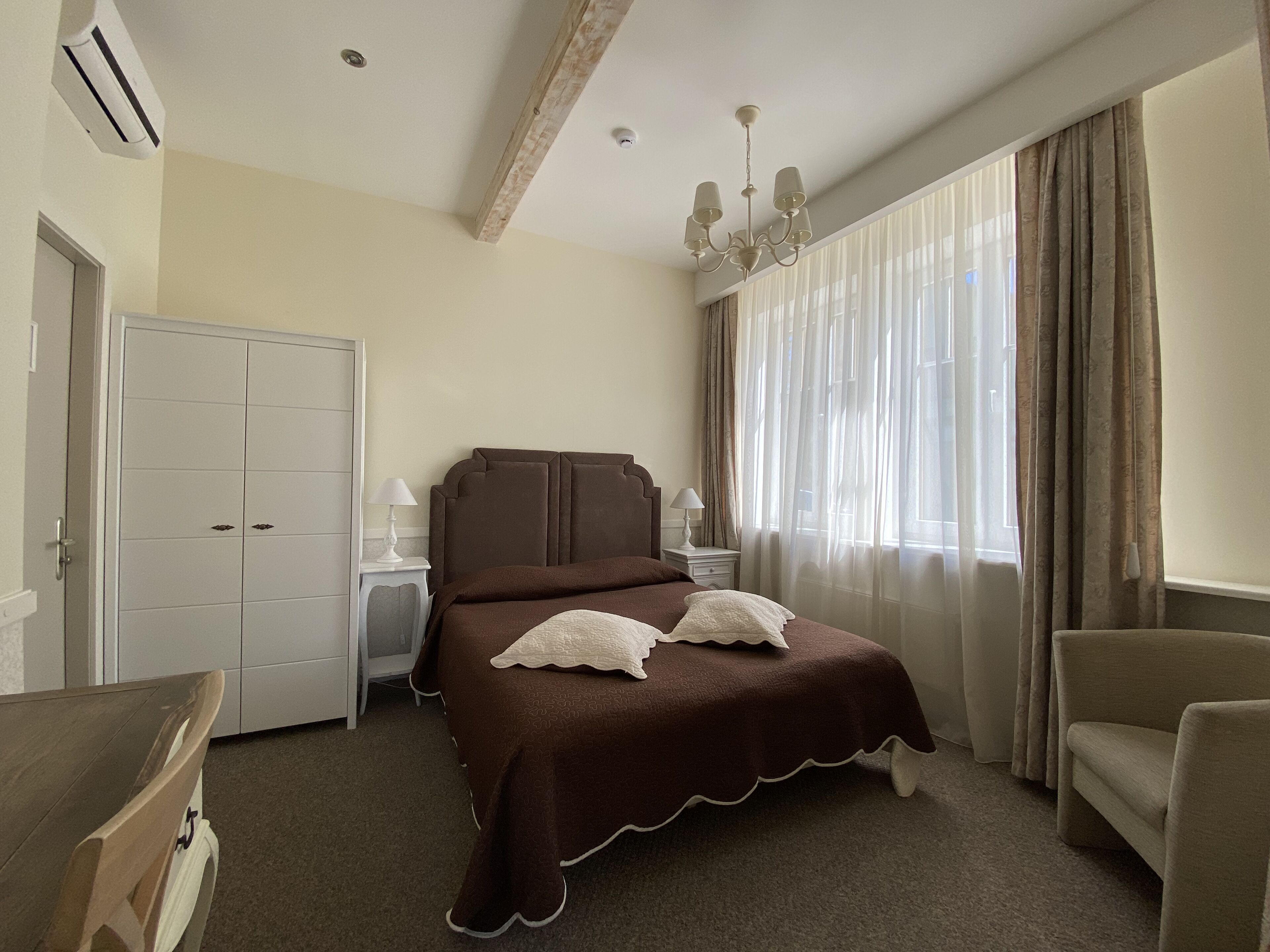 A hotel room with a large bed, a wardrobe, a desk, a chair, and a window with curtains.