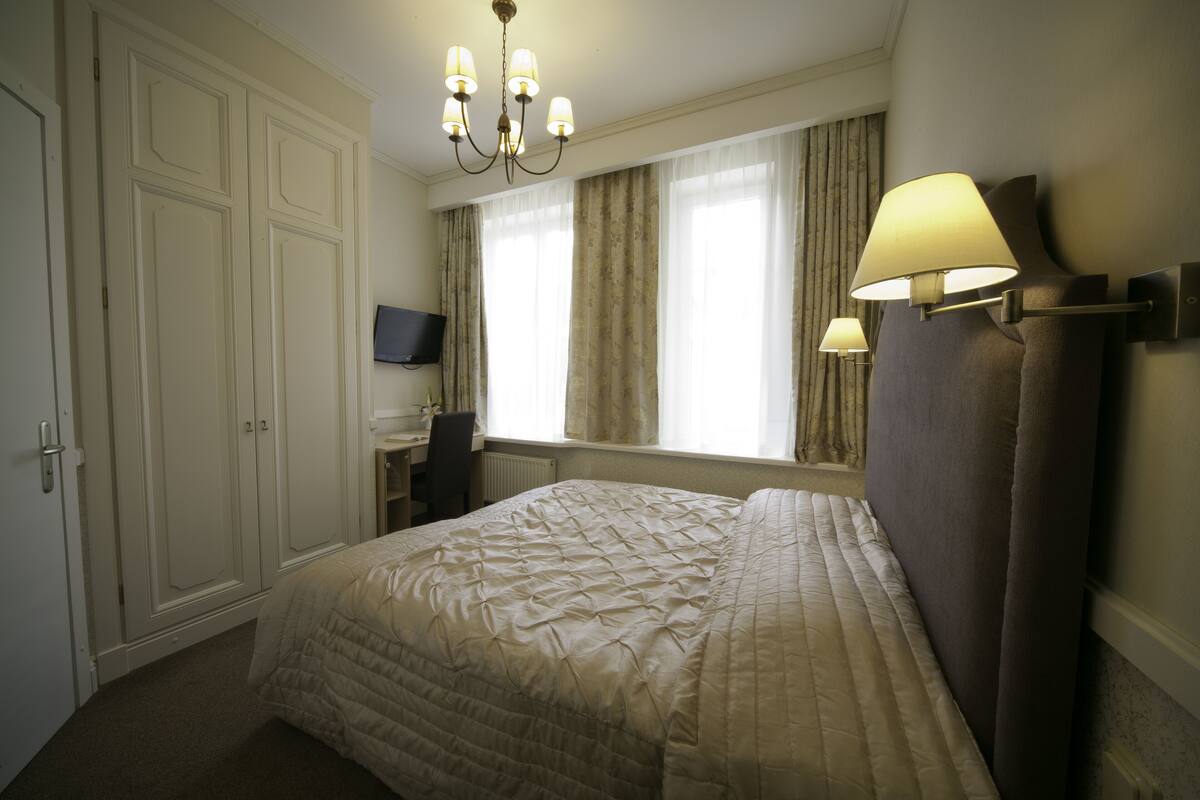 A bedroom with a large bed, a desk, a television, and a chandelier.