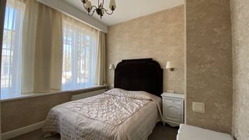 Un dormitorio con cama, mesitas de noche, lámpara, candelabro y ventana con cortinas.