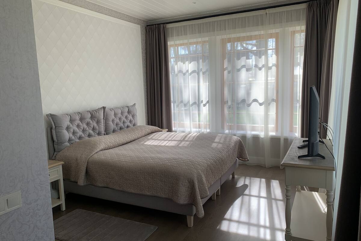 A bedroom with a large bed, a bedside table, a TV, and a window with curtains.