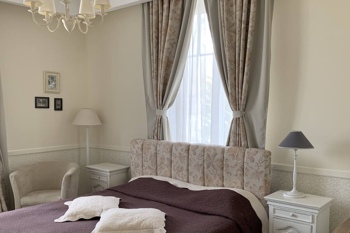 A neatly arranged bedroom with a large bed, a chair, a nightstand, and a lamp.