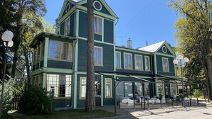 Un edificio verde de dos pisos con ventanas amplias y un área de asientos cubierta al aire libre.