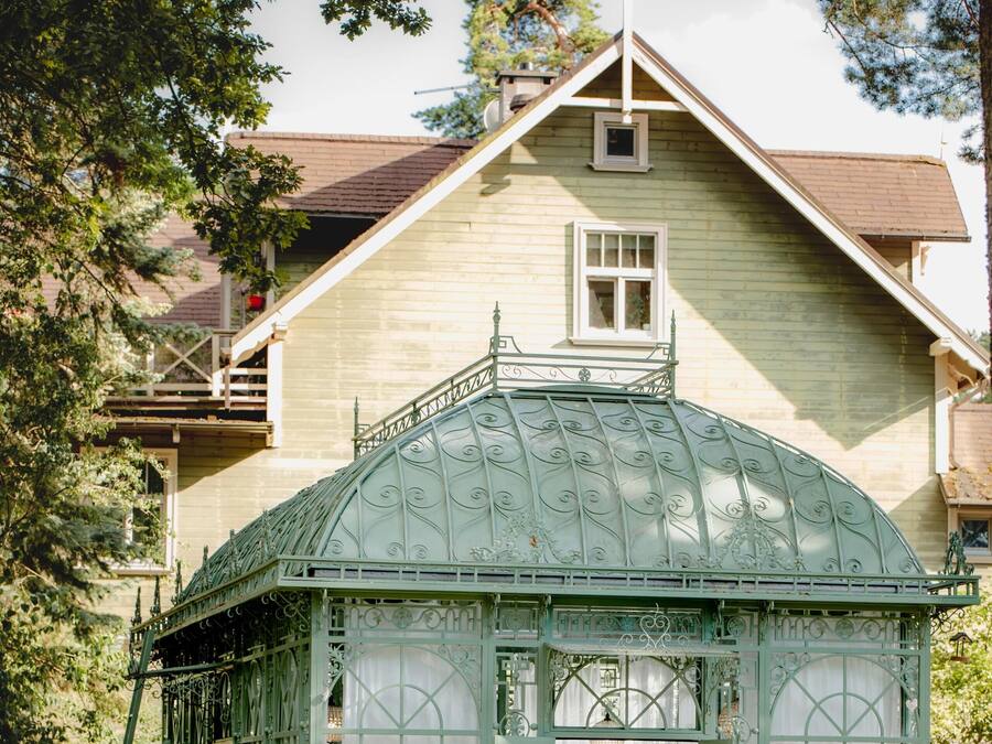 A gazebo with a green roof and white curtains, surrounded by a garden with chess pieces.