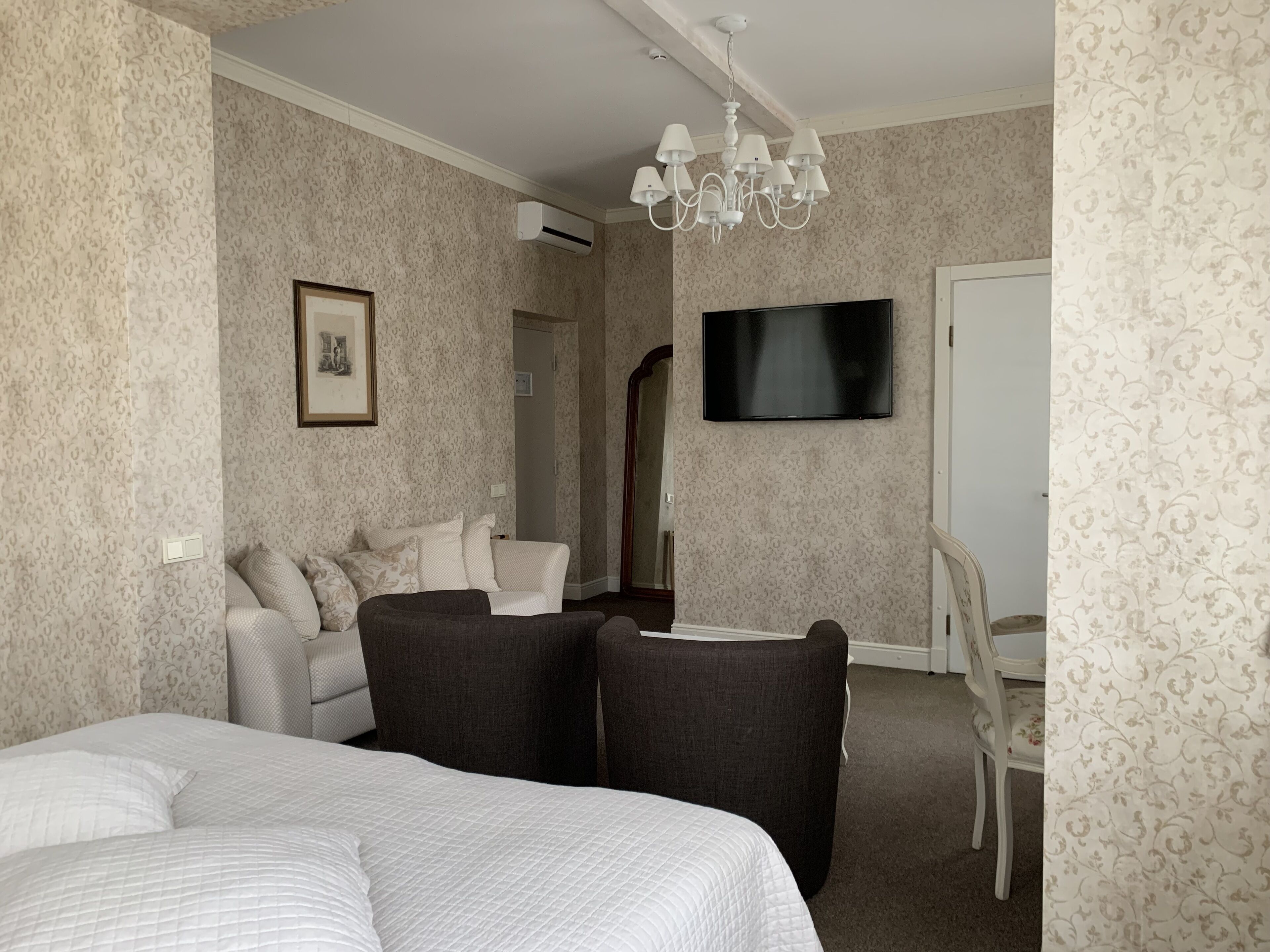 A hotel room with a bed, a sofa, a TV, and a chandelier.