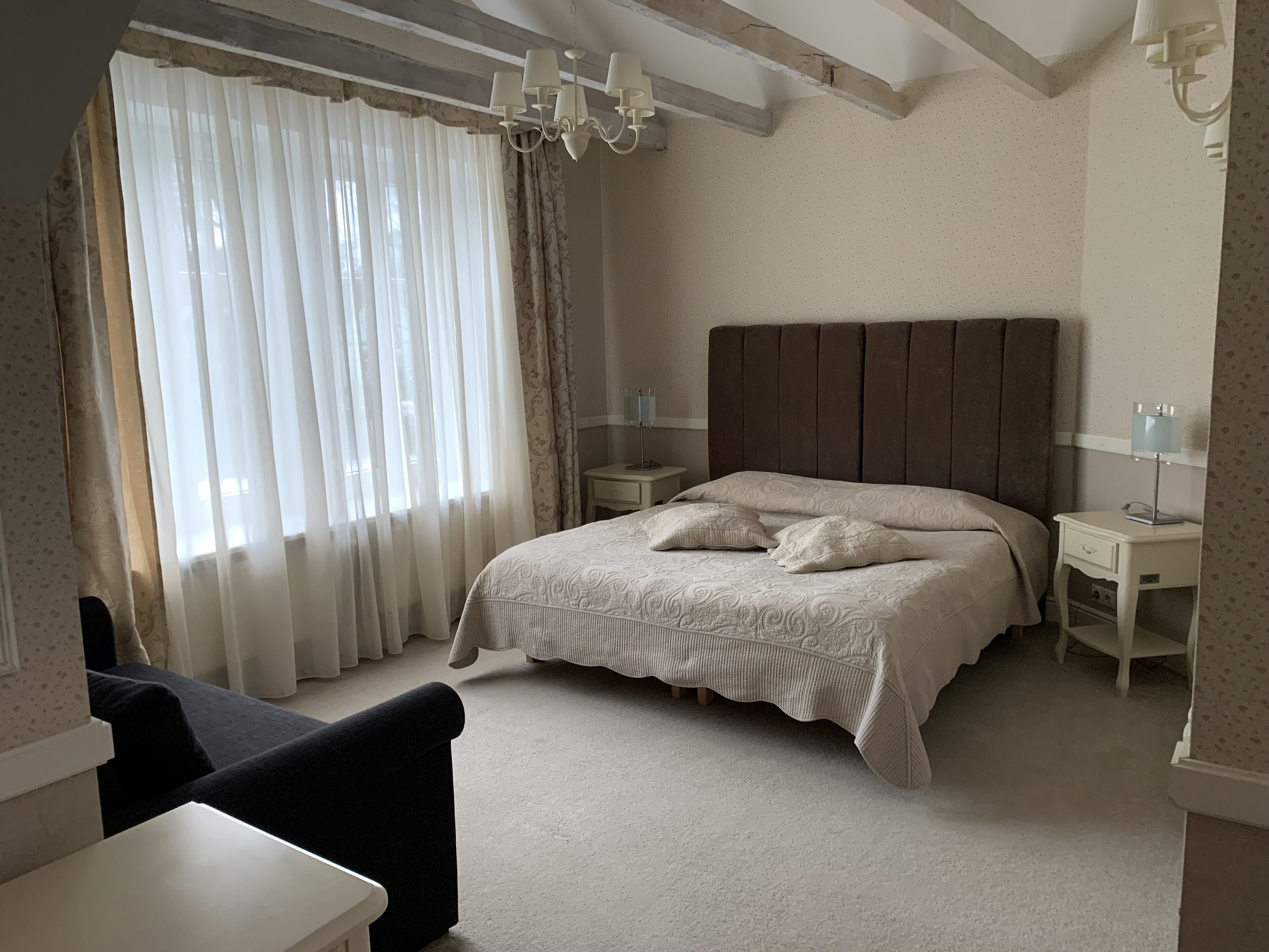 A bedroom with a large bed, two bedside tables, a chair, and a chandelier.