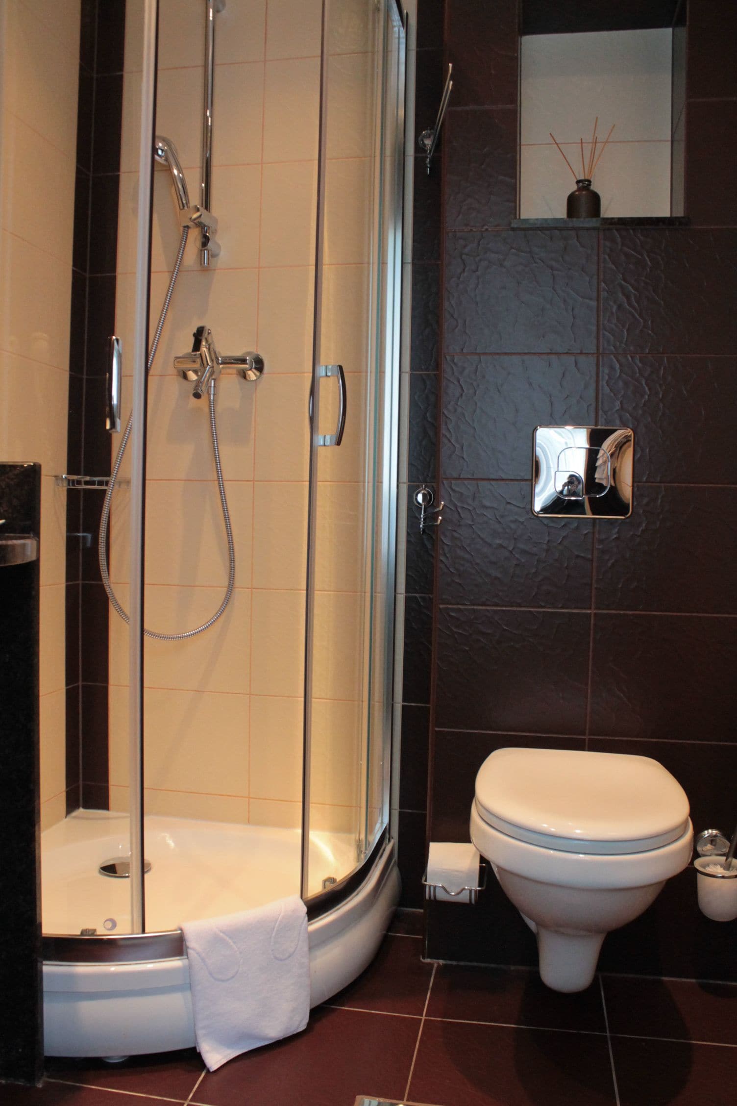 Un baño con ducha envuelta en vidrio, un inodoro y un estante pequeño con un objeto decorativo.