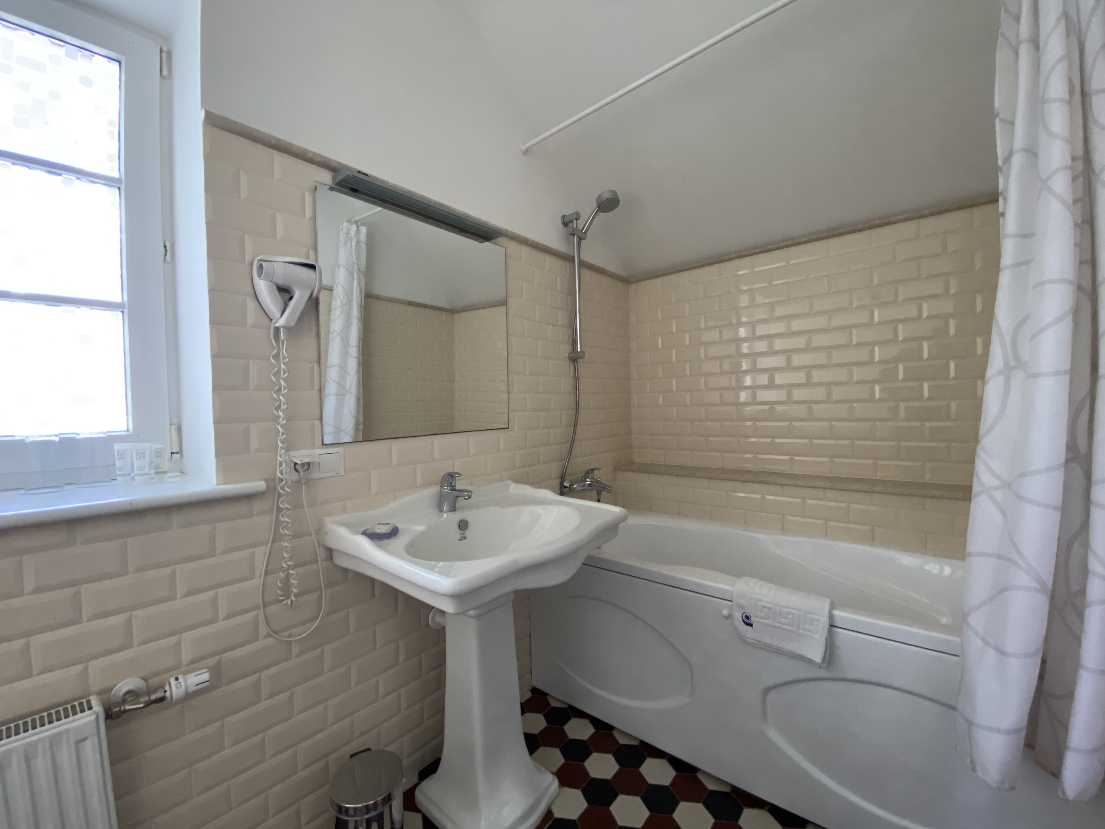 A bathroom with a white sink, a mirror, a shower, and a window.