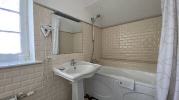 A bathroom with a white sink, a mirror, a shower, and a window.