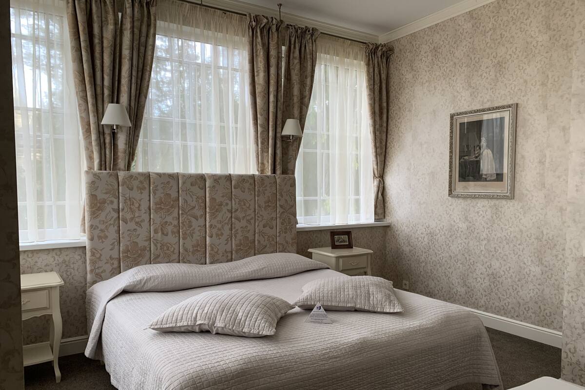 A neatly made bed with a quilted bedspread and pillows, a bedside table with a lamp, and a framed picture on the wall.