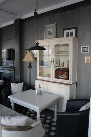 A room with a white table, black chairs, a cabinet with glass doors, a lamp, and a television on the wall. - Villa Joma Hotel (Jurmala)