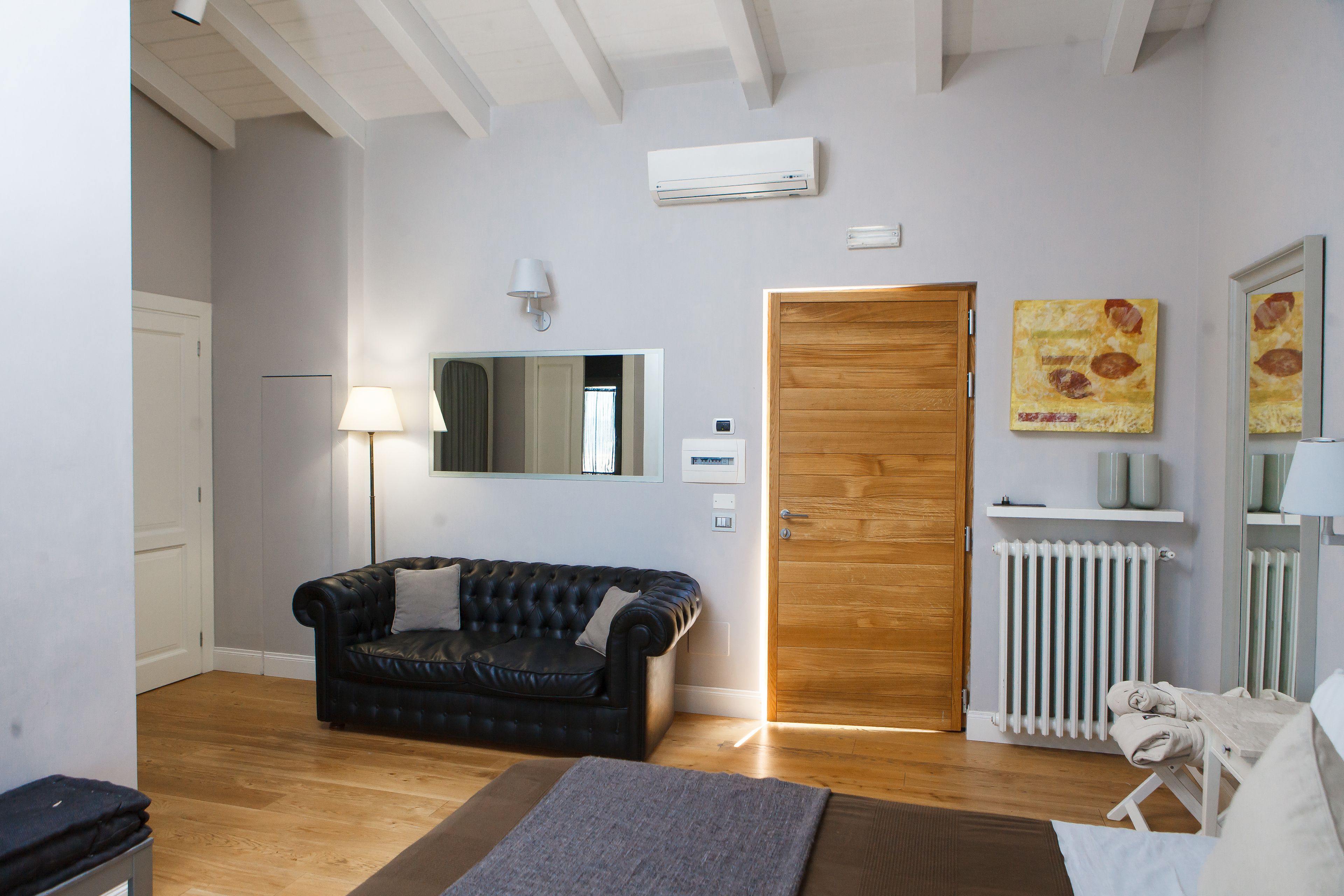 Une pièce avec un canapé en cuir noir, une porte en bois, un radiateur et un miroir au mur.