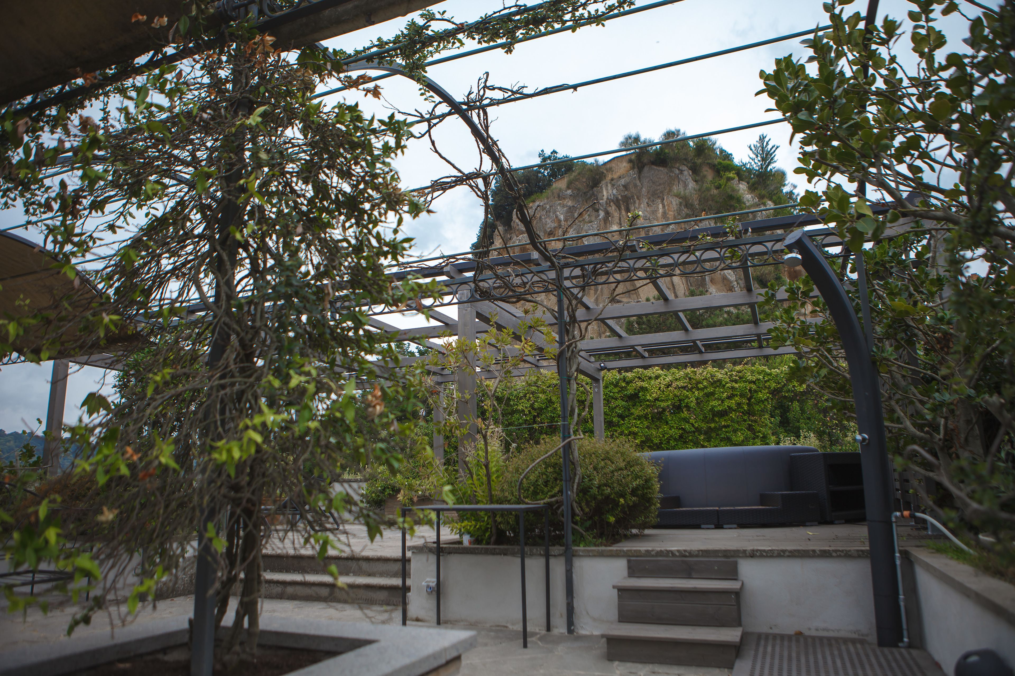 A covered outdoor area with steps leading to a seating area, surrounded by greenery and overlooking a cliff.