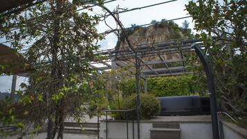 A covered outdoor area with steps leading to a seating area, surrounded by greenery and overlooking a cliff.