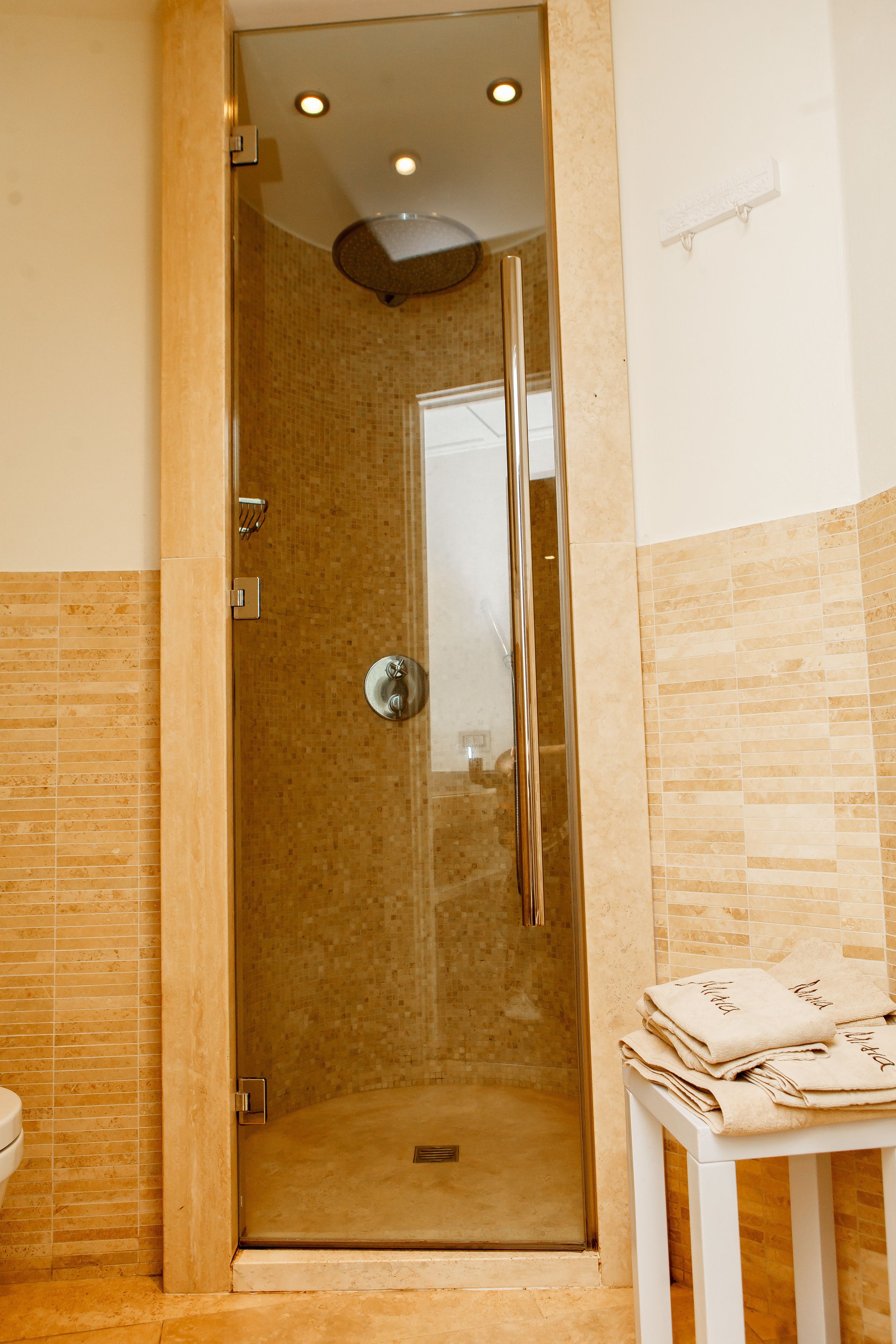 Une cabine de douche fermée par des parois de verre, avec un mur recouvert de carreaux blancs et une petite table sur laquelle sont pliées des serviettes.