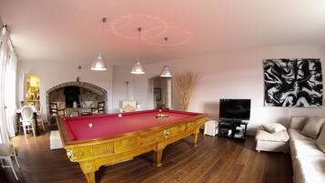A pool table in a living room with a fireplace, a sofa, and a TV.