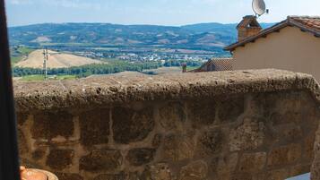 A stone wall with a view of a town, a rustic bench, and a large clay pot.