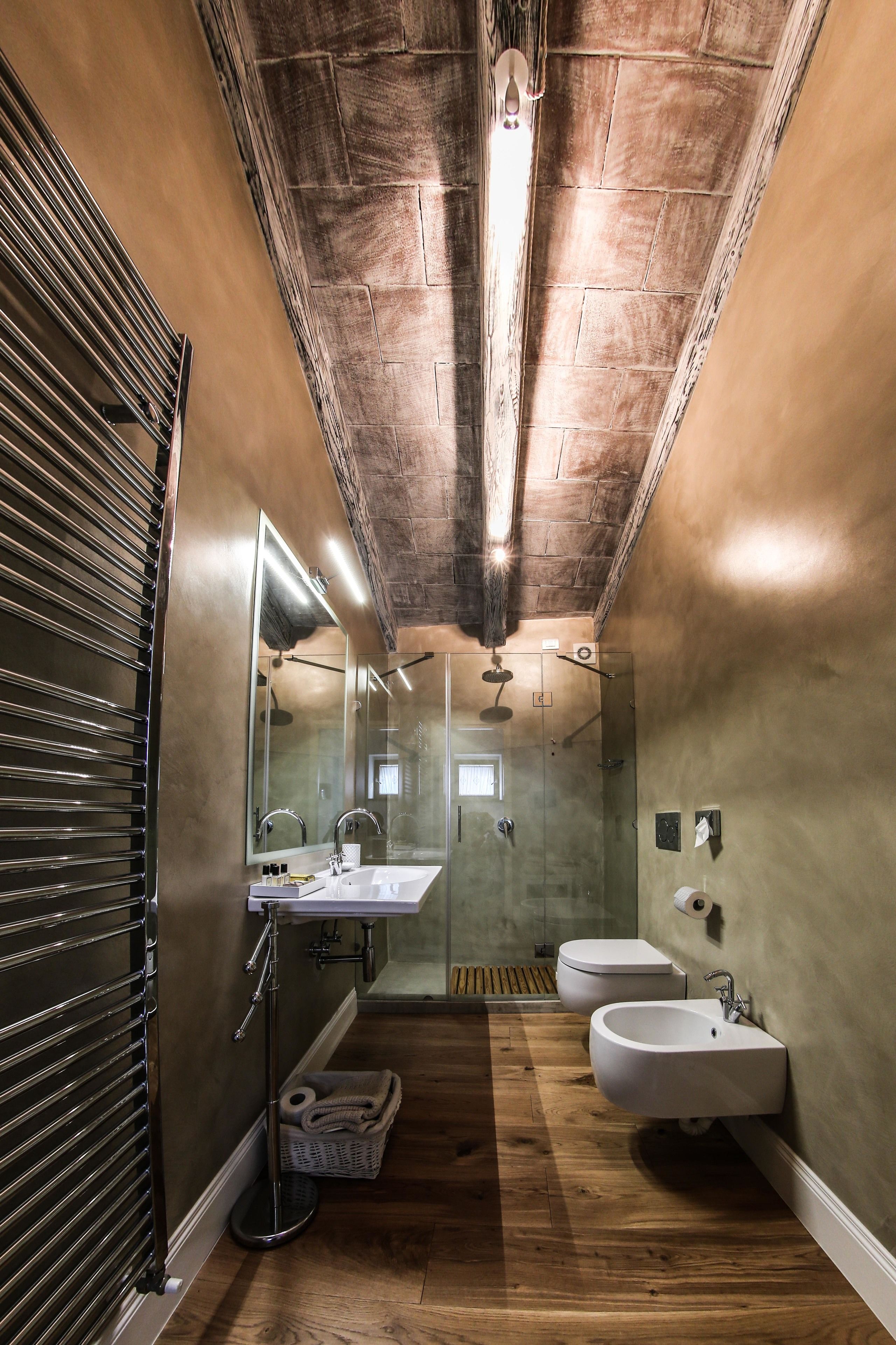 A narrow bathroom with wooden flooring, a large mirror, two sinks, and a shower area.