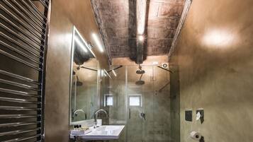 A narrow bathroom with wooden flooring, a large mirror, two sinks, and a shower area.