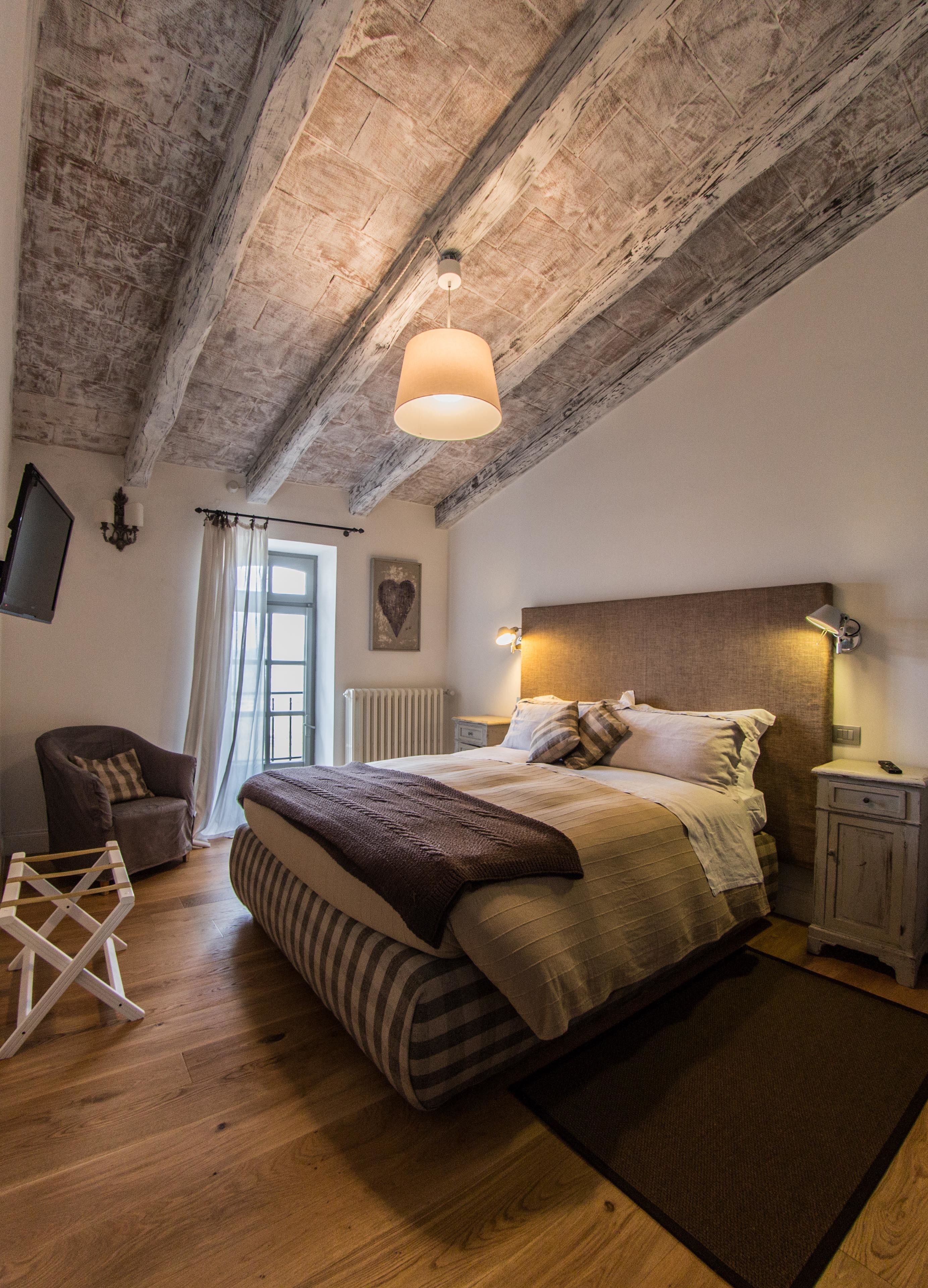 Un dormitorio con techo de madera, una cama con ropa de cama a rayas, una mesita de noche con lámpara y una silla.