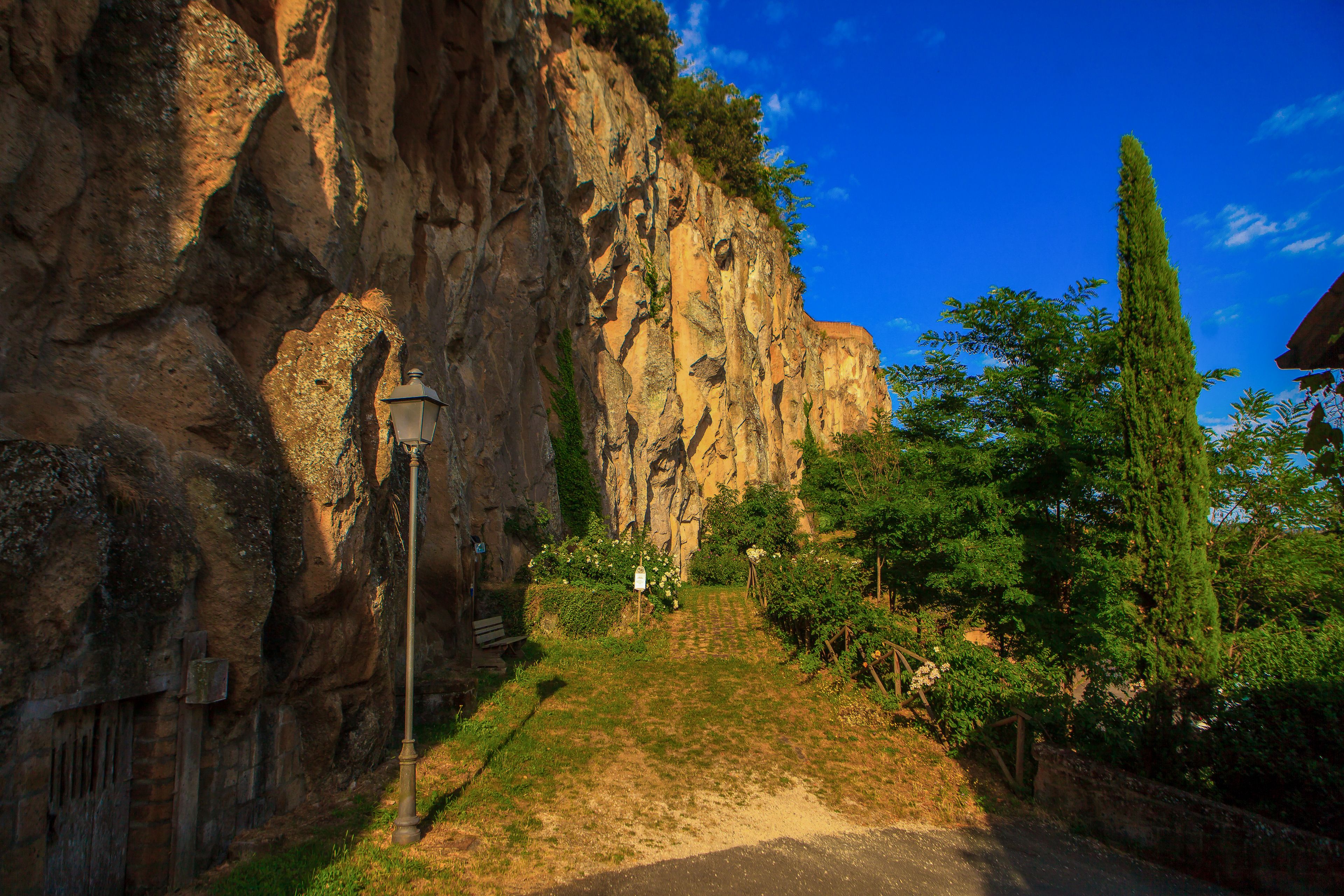 A pathway leading up a rocky cliff with a lamp post and a sign.