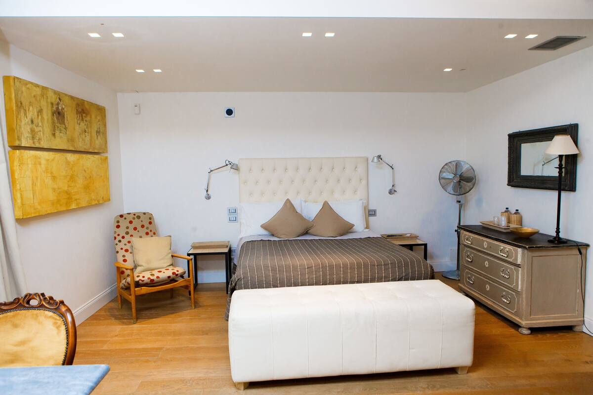 A bedroom with a bed, a chair, a dresser, and a lamp.