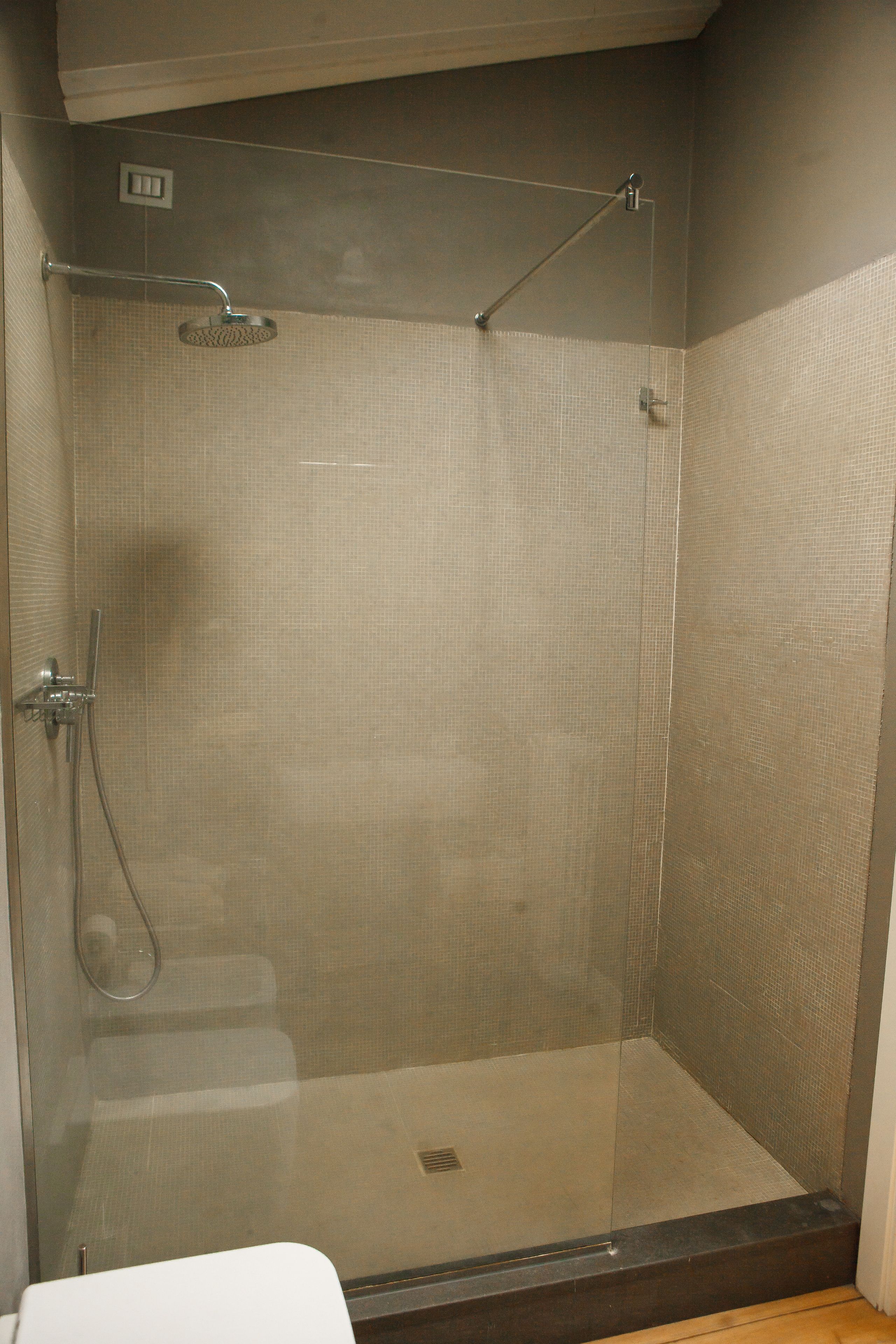 A glass-enclosed shower stall with a handheld showerhead and a wall-mounted faucet.