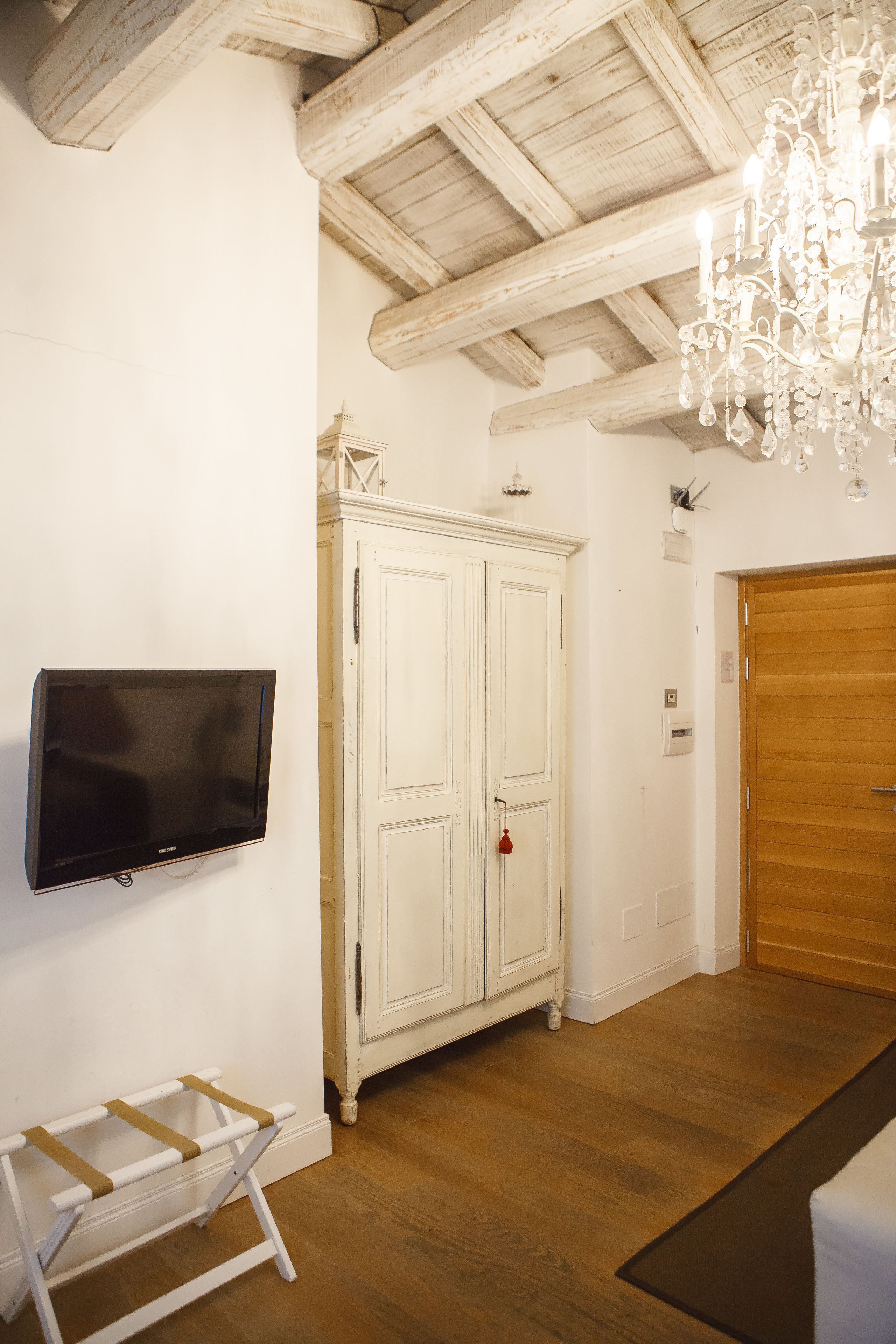 Une pièce avec un plafond en bois, une armoire blanche, un téléviseur fixé au mur et une porte en bois.