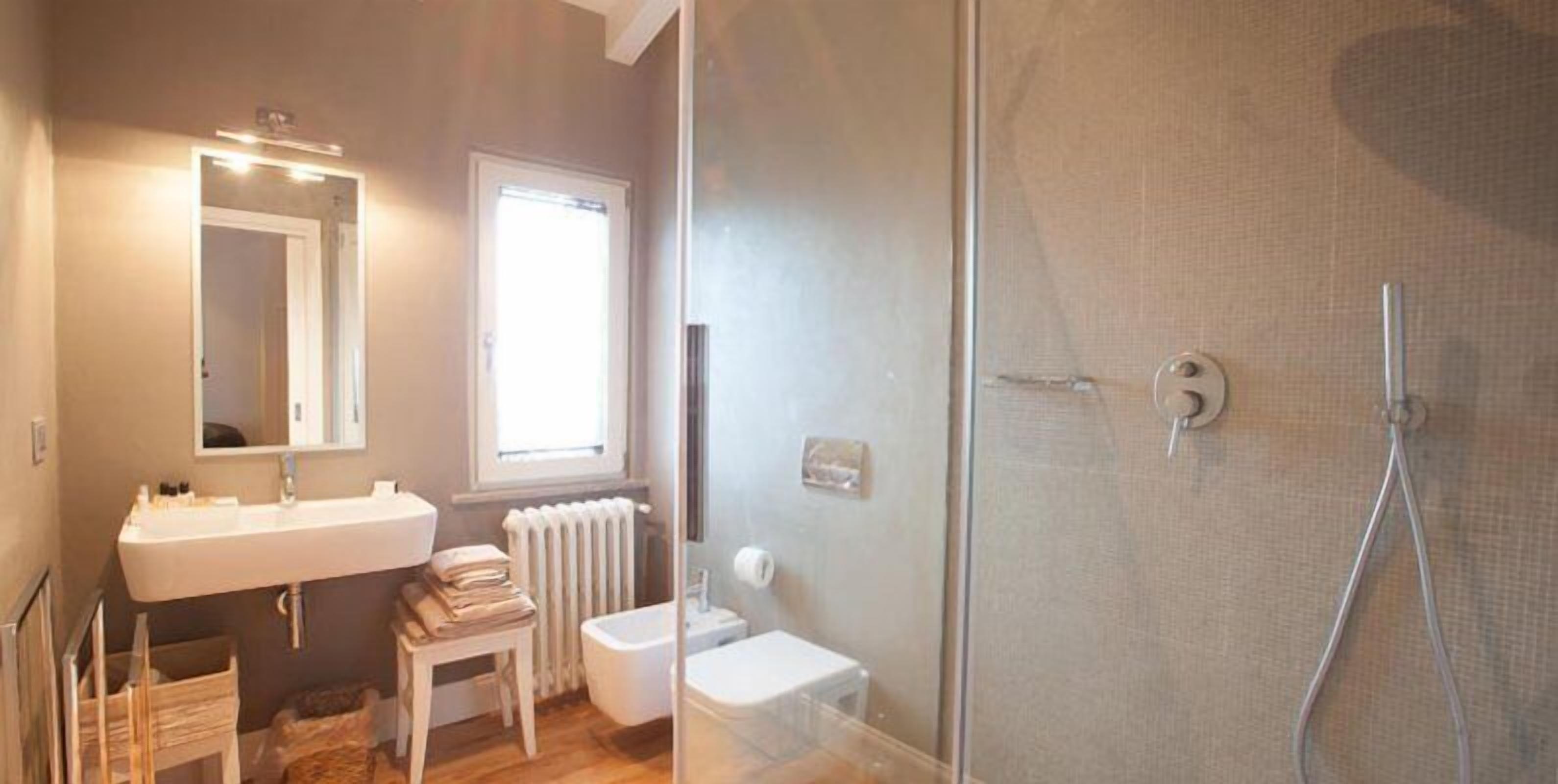 Une salle de bain avec un lavabo blanc, un miroir et des toilettes, une douche en verre et un radiateur.