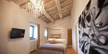 Un dormitorio con cama, televisión, candelabro y una pintura.