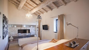 A modern bedroom with a wooden ceiling, a bed, a bedside table with a lamp, a TV, and a bathroom with a shower and a bathtub. - Misia Country Resort (Orvieto)