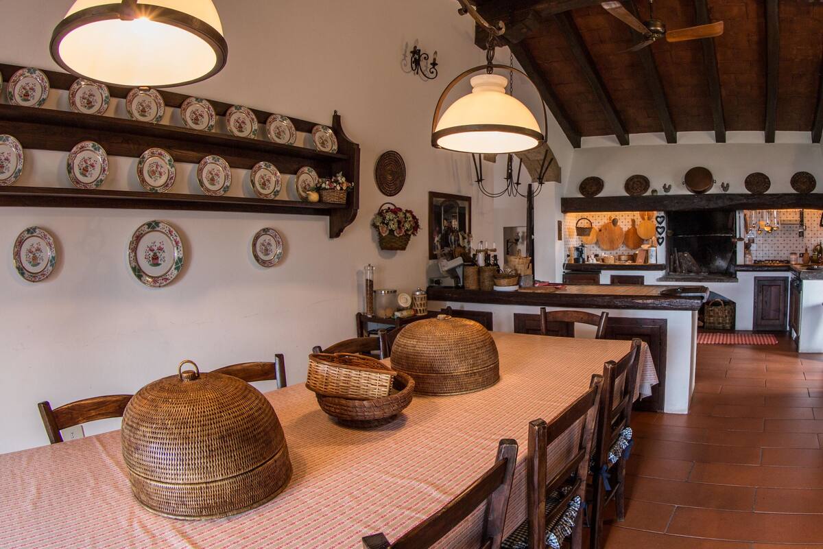 A dining area with a long table, wicker baskets, and a hanging light fixture.