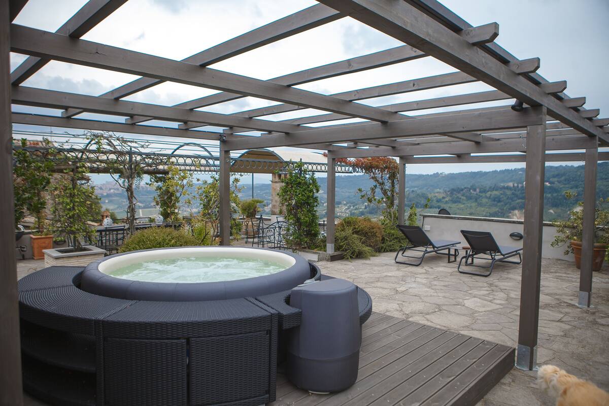 A hot tub and lounge chairs under a pergola with a view of the mountains.