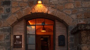 A stone building entrance with a glass door, a signboard, and a small garden area with pink flowers. - Misia Country Resort (Orvieto)