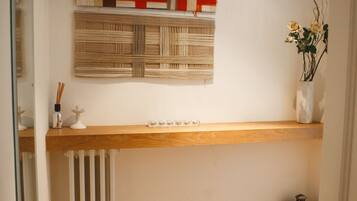 A hallway with a wooden floor, a radiator, a shelf with a decorative piece, and a wall-mounted artwork.