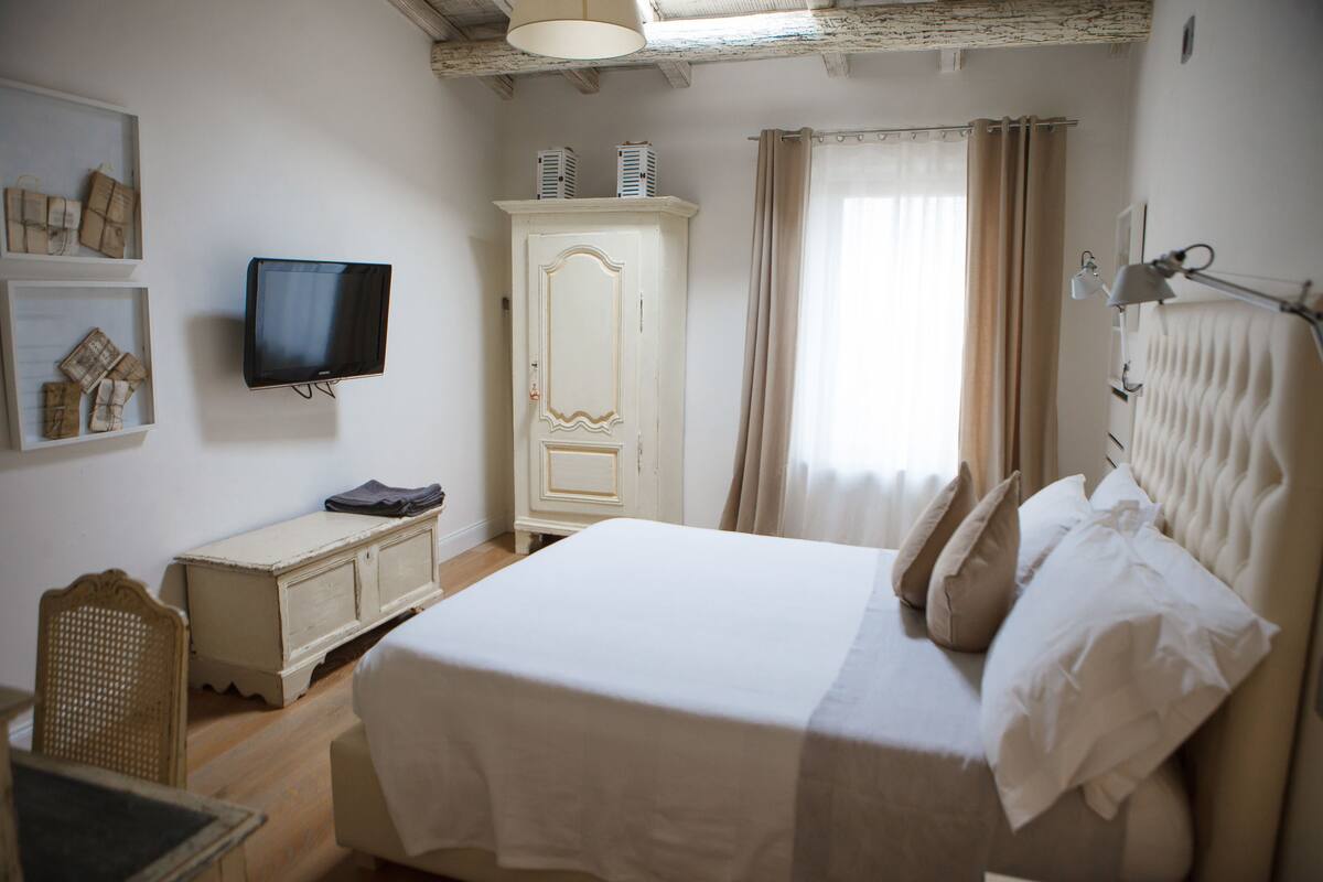 A bedroom with a bed, a television, a wardrobe, and a window with curtains.
