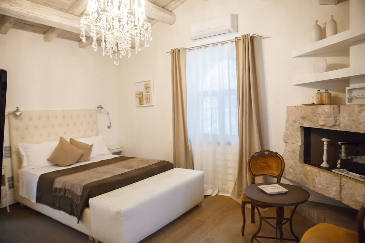 A bedroom with a bed, a chair, a fireplace, and a chandelier.